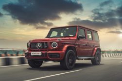the red mercedes g class is driving down the road.
