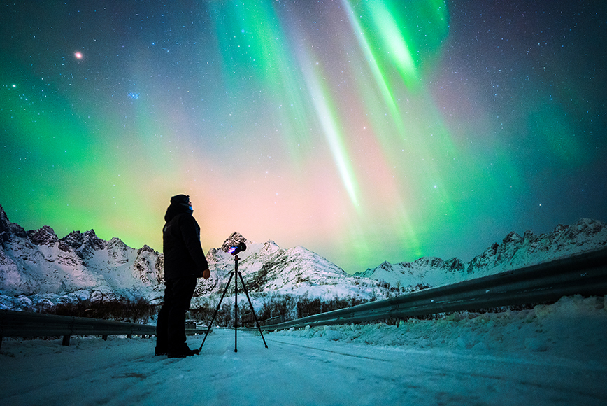 A man is standing in front of the aurora borealis in norway.