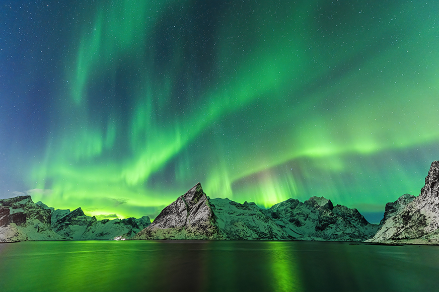 A green aurora bore over a lake and mountains.