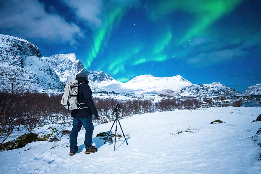 A man is standing in the snow looking at the aurora borealis.