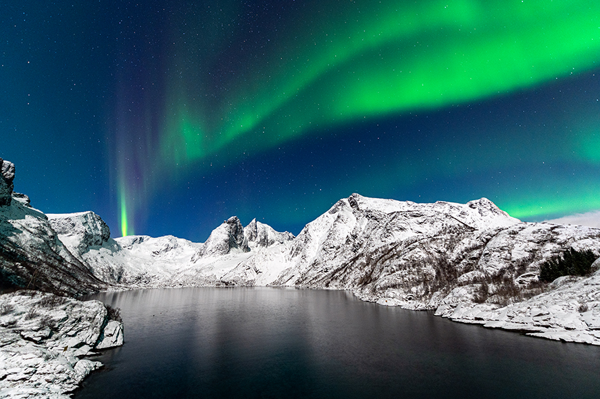 The aurora borealis lights up the sky over snowy mountains.