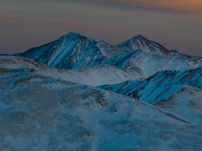 A mountain range with snow covered peaks at dusk.