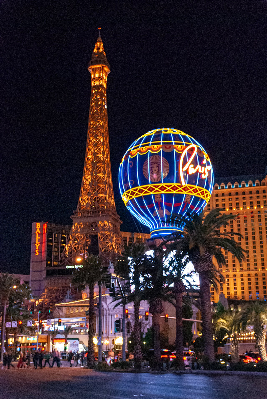 Las vegas at night with the eiffel tower and palm trees.