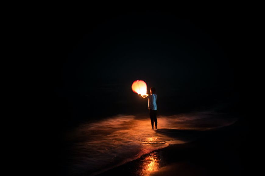 A man standing on the beach holding a fire torches.