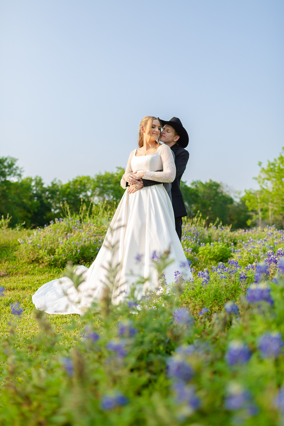 A bride and groom embracing in a field of flowers.